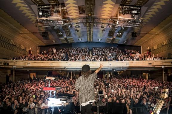 Back of a performer on stage of a full auditorium concert