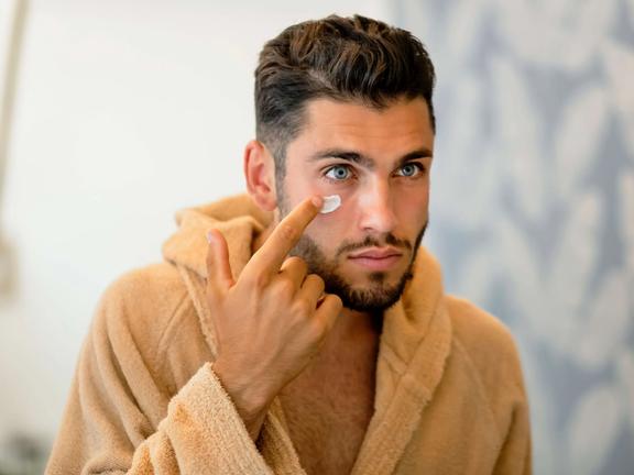 reflection of a man in a mirror applying cream to his face