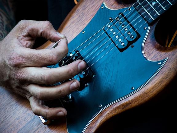 hand strumming a vintage guitar with a guitar pick