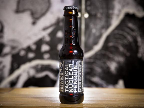 Close up of BrewDog Tactical Nuclear Penguin beer bottle set on a wooden bar