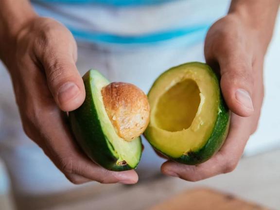 pair of hands holding an avocado in half